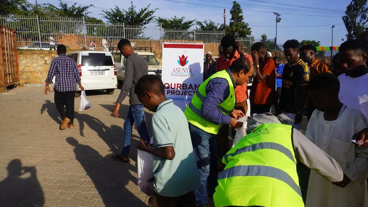 Helfer in Warnwesten geben Tüten an eine wartende Menschengruppe aus, im Hintergrund ein Banner des Qurban-Projekts in Uganda