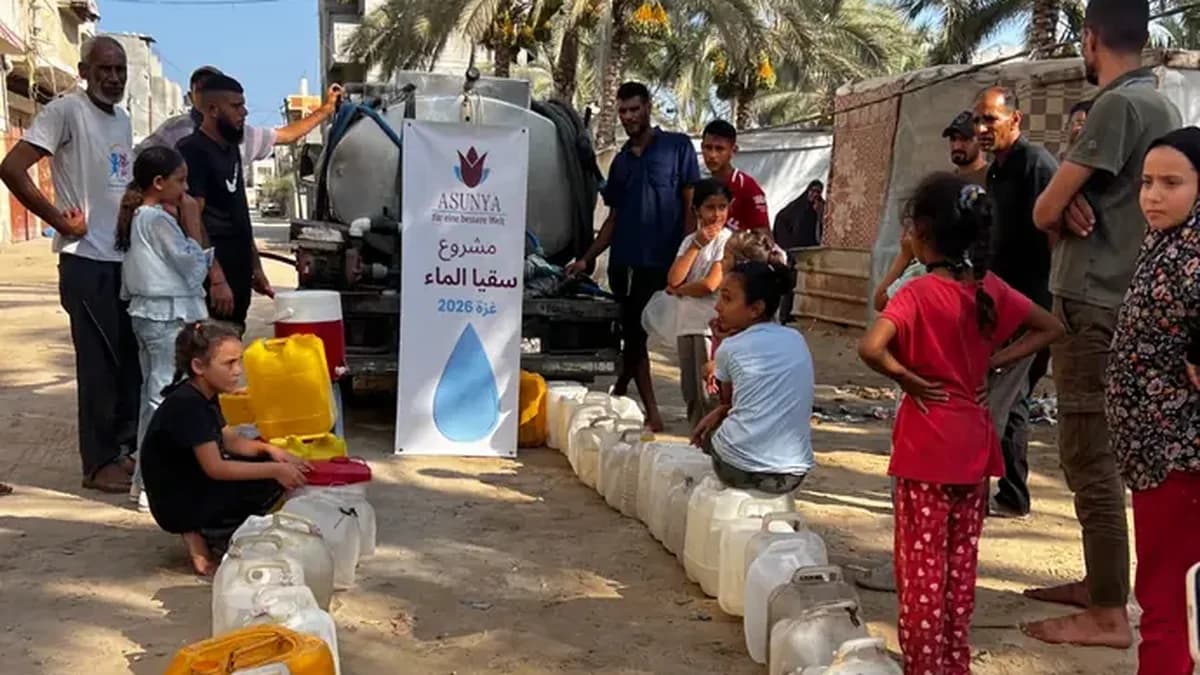 Menschen in Gaza stehen mit Wasserkanistern vor einem Tankwagen, davor ein Banner von Asunya zum Wasserprojekt 2026