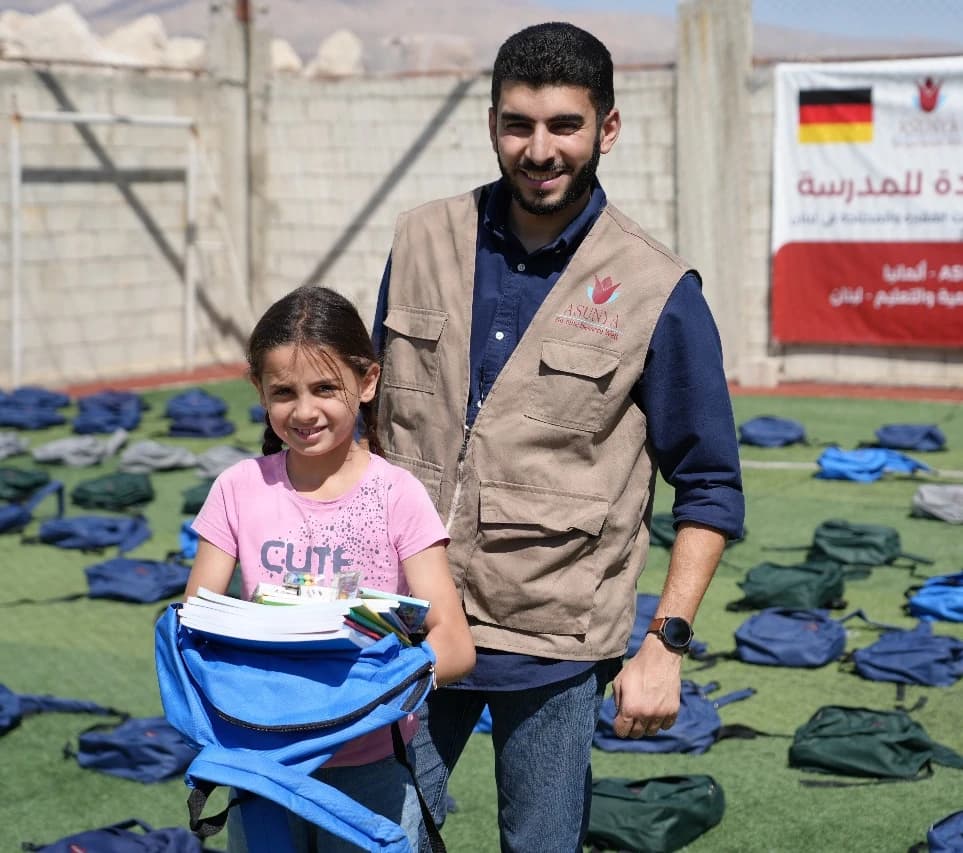 Ein Asunya-Mitarbeiter übergibt einem Mädchen einen Schulrucksack bei der Verteilung im Projekt „Rückkehr zur Schule“ im Libanon